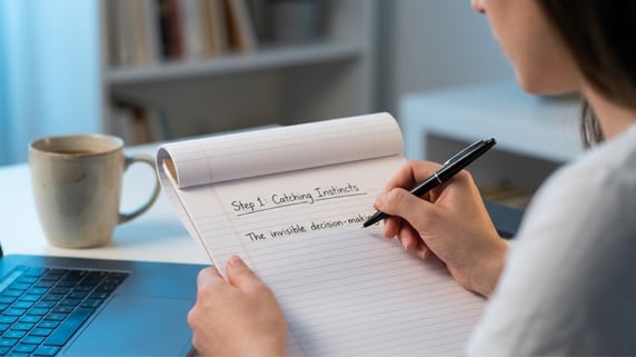 Small business owner catches an 'invisible process' by writing down a judgment call instinct on a lined notepad with a black pen, as defined by a revenue growth consultant for small business.